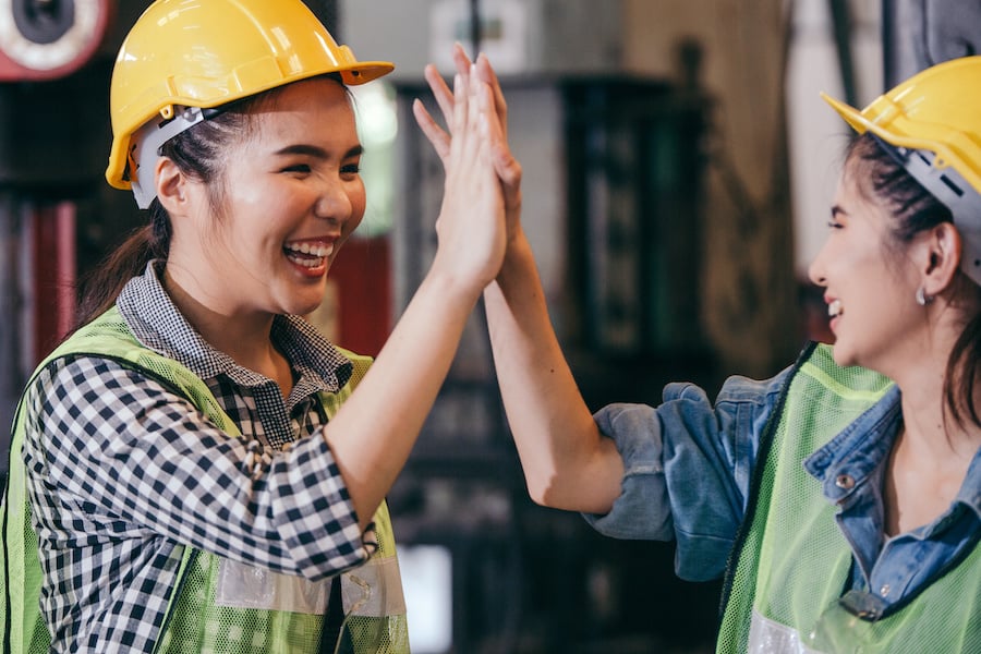 Two female workers wearing hardhats and reflective vest high-fiving